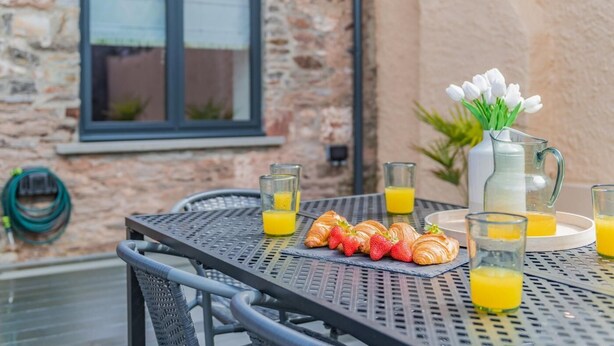Ein Tisch mit Croissants, Erdbeeren und Gläsern Orangensaft, vor einer Steinwand mit einem Fenster.