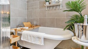Ein modernes Badezimmer mit einer freistehenden Badewanne, einem Holzkosmetikschrank, einem Handtuchhalter und einer Topfpflanze.