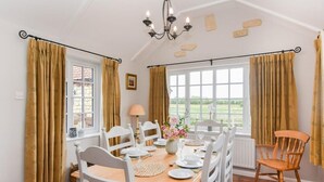 A dining room with a wooden table set for four, white chairs, a chandelier, and large windows with curtains. - 3 Bed in Lincoln (oc-90396) (Washingborough)