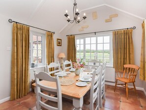 Ein Esszimmer mit Holztisch, gedeckt für vier Personen, weißen Stühlen, einer Chandelüster und großen Fenstern mit Vorhängen.