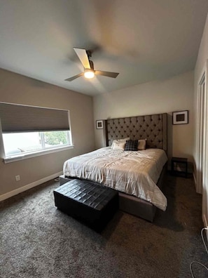 Una camera da letto con un letto, una ventola a soffitto, una finestra e un piccolo tavolo.