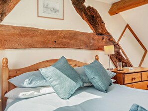 A bedroom with a wooden headboard, a bed with blue bedding, a bedside table with a lamp, and a mirror.