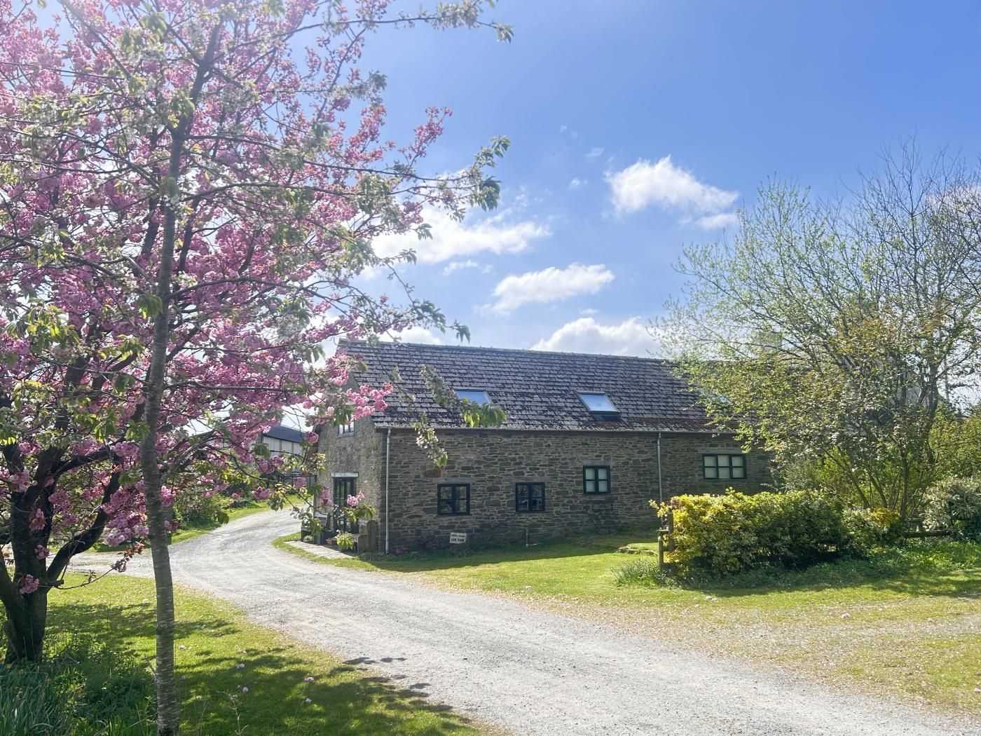 A stone building with a gravel driveway and a tree with pink blossoms.