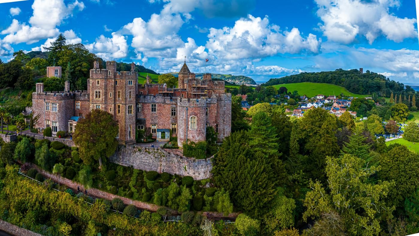 A castle-like building with multiple towers and a surrounding moat, set in a lush green landscape.