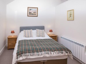 Ein Schlafzimmer mit einem Bett, zwei Nachttischen, einem Heizkörper und zwei gerahmten Bildern an der Wand.