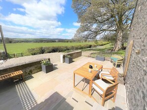 Une terrasse extérieure avec une table et des chaises, un mur en pierre et une vue sur un champ verdoyant.