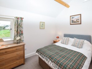 Une chambre à coucher avec un lit, une commode, une fenêtre avec des rideaux, une lampe de chevet, un tableau encadré et une vue sur l’extérieur.