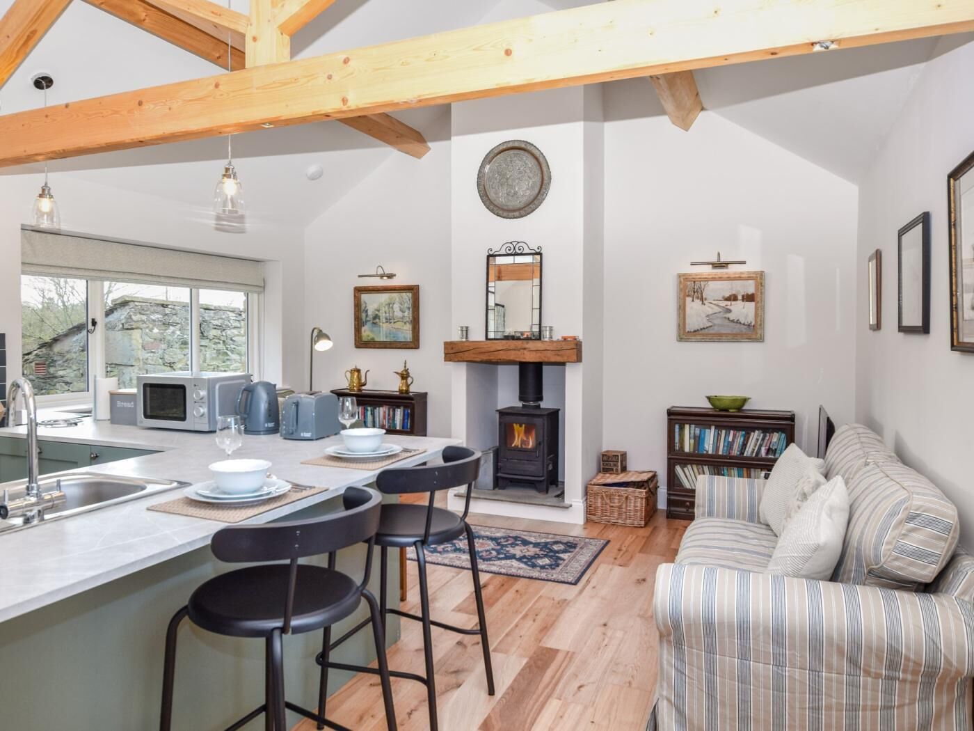 A modern kitchen with a central island, bar stools, a fireplace, and a cozy seating area with a striped sofa.