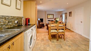 Een keuken met een wasmachine, een eethoek met stoelen, en een woonkamer met een bank en een televisie.