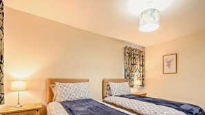 Een slaapkamer met twee bedden, een nachtkastje met lamp, een houten dressoir en een plafondlamp.