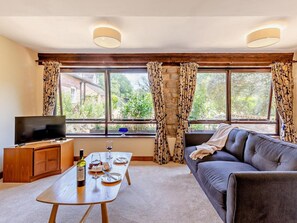 A living room with a sofa, a TV, a wooden table with a bottle and glasses, and a window with curtains. - 2 Bed in Kidderminster (oc-90642) (Stottesdon)