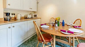 Une cuisine compacte avec des meubles blancs, un plan de travail en bois, une table à manger pour quatre personnes et une machine à café.