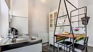 A compact kitchen with a built-in stove, a sink, and a small dining area with a metal chair and table. - 1 Bed in Keswick (oc-90646) (Keswick)