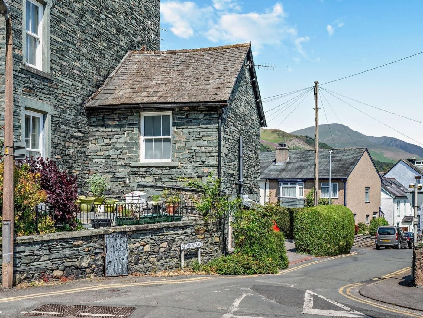 A stone building with a pitched roof, a window, and a street sign indicating 'Corn Street.'