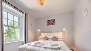 A neatly made bed with white linens, a large window with curtains, a colorful abstract painting on the wall, and a sign with a motivational quote. - 1 Bed in Keswick (oc-90646) (Keswick)