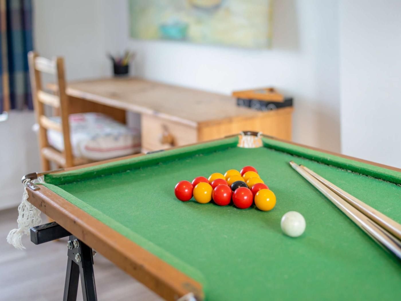 A pool table with billiard balls and cues, a wooden chair, and a small table with a plant.