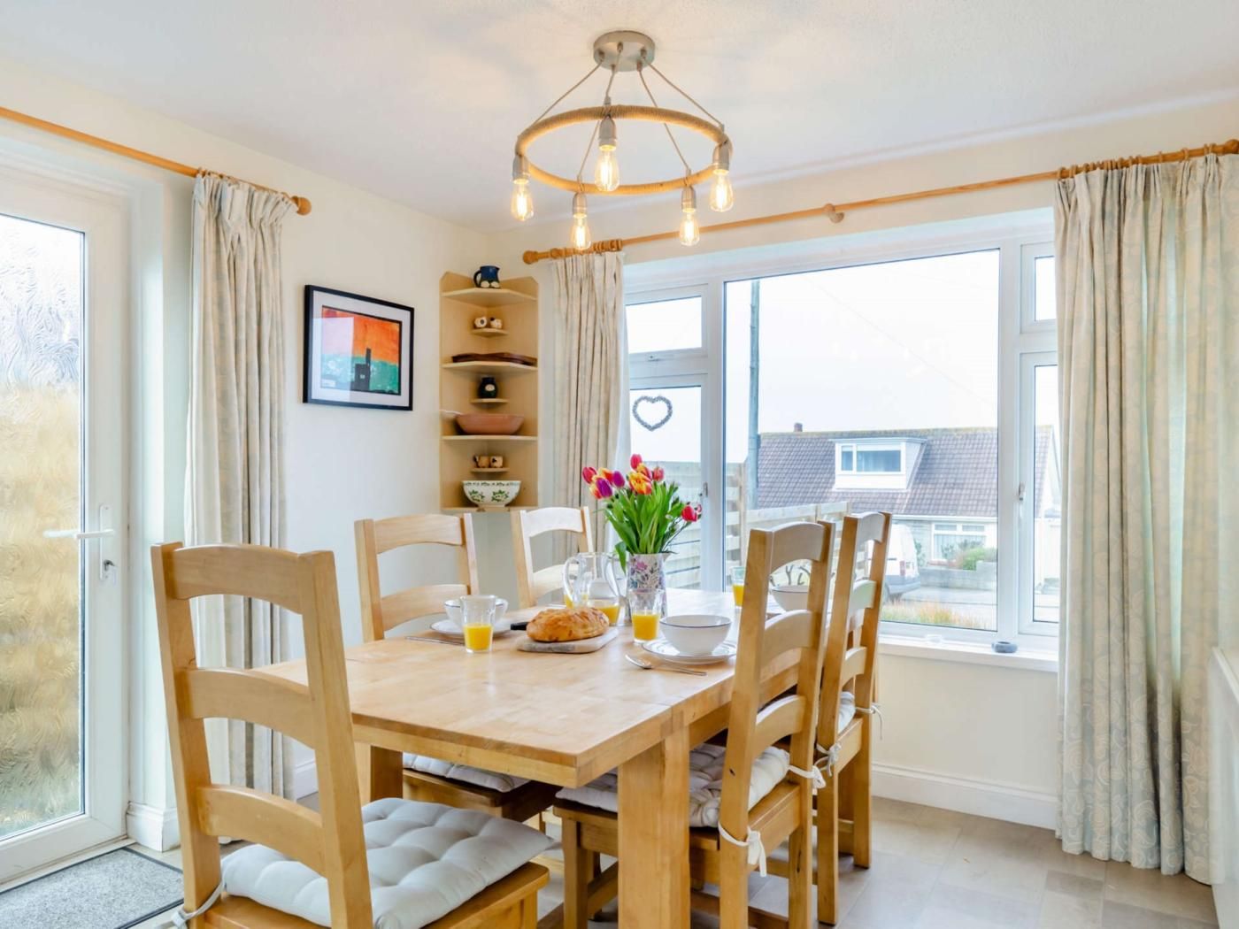 A dining area with a wooden table, chairs, a chandelier, and a view of the outside.