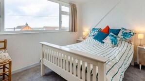 Ein Schlafzimmer mit Bett, Fenster, Sessel und Nachttisch.