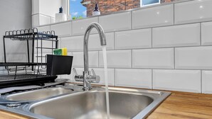 Een RVS spoelbak met een moderne kraan, een afdruiprek en een raam met uitzicht op een bakstenen gebouw.