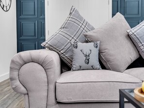 A grey upholstered sofa with multiple cushions, including a patterned one with a deer head, against a blue door. - Family lux home/6-car drv/ pool table/projector/ (Chadderton)