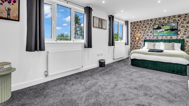 Een slaapkamer met een groot bed, een radiator, een raam met gordijnen, en een muur met een bloemenmotief.