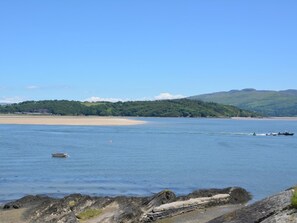 A coastal landscape with a sandy beach, calm water, and a small boat. - 3 Bed in Porthmadog (oc-90615) (Borth-y-Gest)