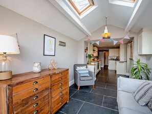 A modern living room with a wooden dresser, a grey sofa, and a dining area with a kitchen in the background. - 3 Bed in Porthmadog (oc-90615) (Borth-y-Gest)