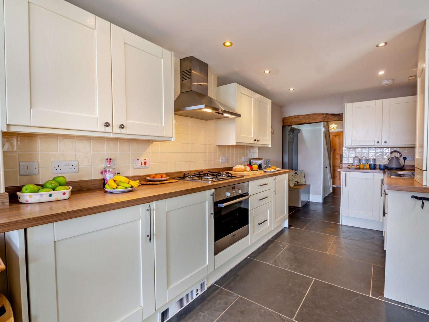 A modern kitchen with white cabinets, a central island with fruits, a stove, and a built-in oven.