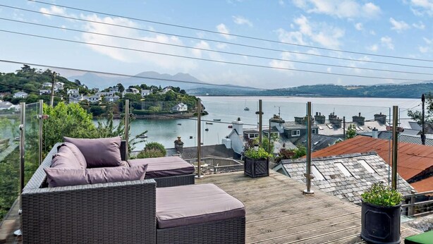 Um terraço com mobiliário de vime, vista para um corpo d'água e edifícios ao longe.
