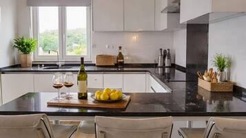 A modern kitchen with a large island, bar stools, and a view of greenery outside.