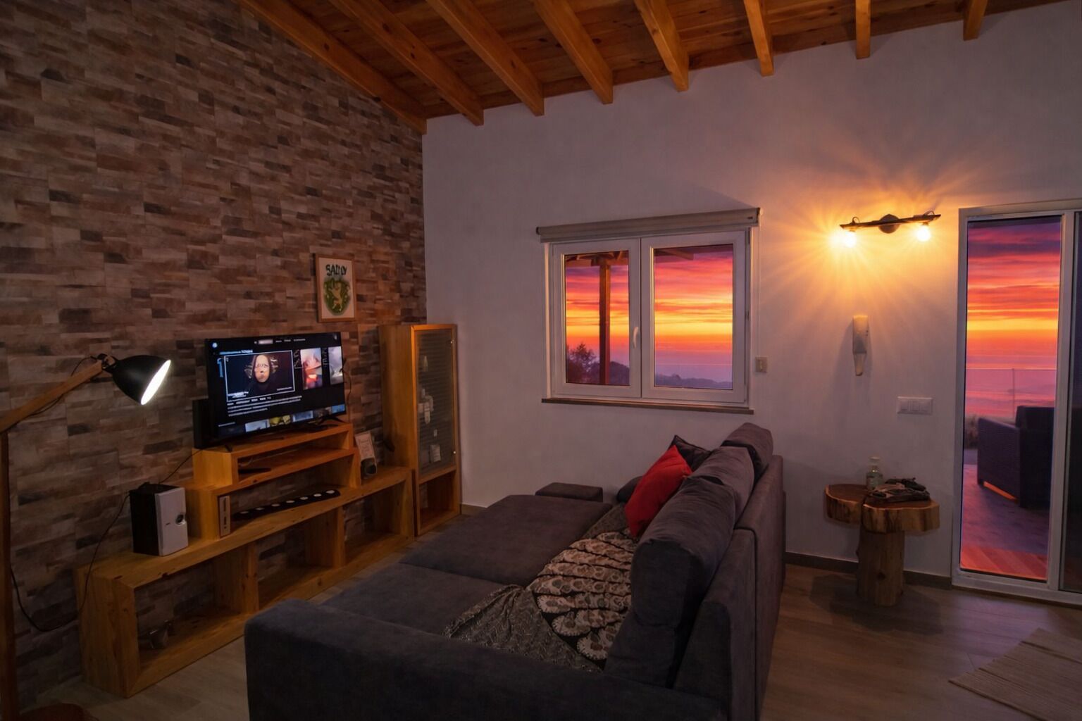 Ein Wohnzimmer mit Fernseher, Holzmöbeln, einer Couch und Blick auf einen Sonnenuntergang durch ein Fenster.