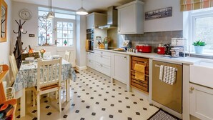 A kitchen with a dining area, a clock, a window with a tree decoration, and a red appliance on the counter. - 1 Bed in Whitby (oc-90699) (Fylingdales)