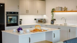 A modern kitchen with a central island, white cabinetry, a built-in oven, and a microwave. - 3 Bed in Holsworthy (oc-90721) (Holsworthy)