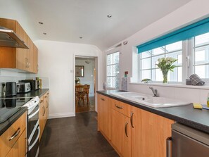 A modern kitchen with wooden cabinets, a black countertop, and a window with a view. - 3 Bed in Sheringham (oc-90701) (Sheringham)