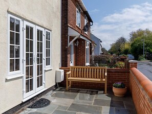 A residential property with a brick exterior, a white-framed window, a wooden bench, and a potted plant. - 3 Bed in Sheringham (oc-90701) (Sheringham)
