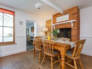 A dining area with a brick fireplace, wooden chairs, a table set for four, and a window with blinds. - 3 Bed in Sheringham (oc-90701) (Sheringham)