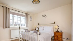 Een slaapkamer met een bed, nachtkastjes, een dressoir, een raam met gordijnen, een radiator en een wandlamp.