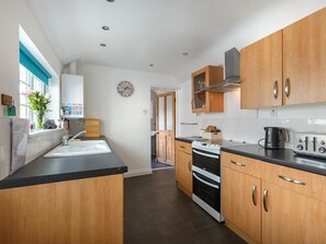 A modern kitchen with wooden cabinets, a black countertop, and a stainless steel range hood. - 3 Bed in Sheringham (oc-90701) (Sheringham)