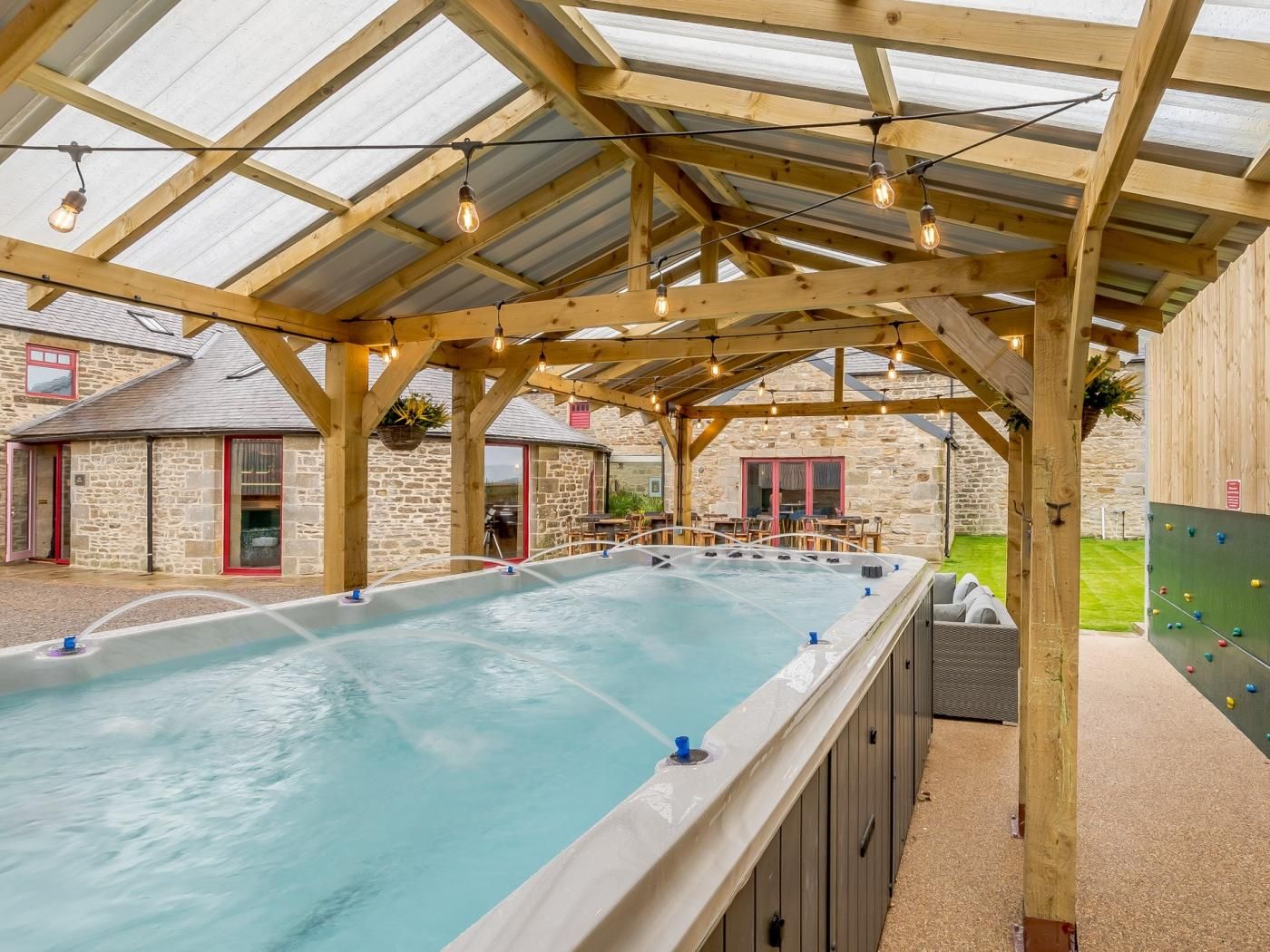 A hot tub area with a wooden pergola overhead, stone walls, and a climbing wall.