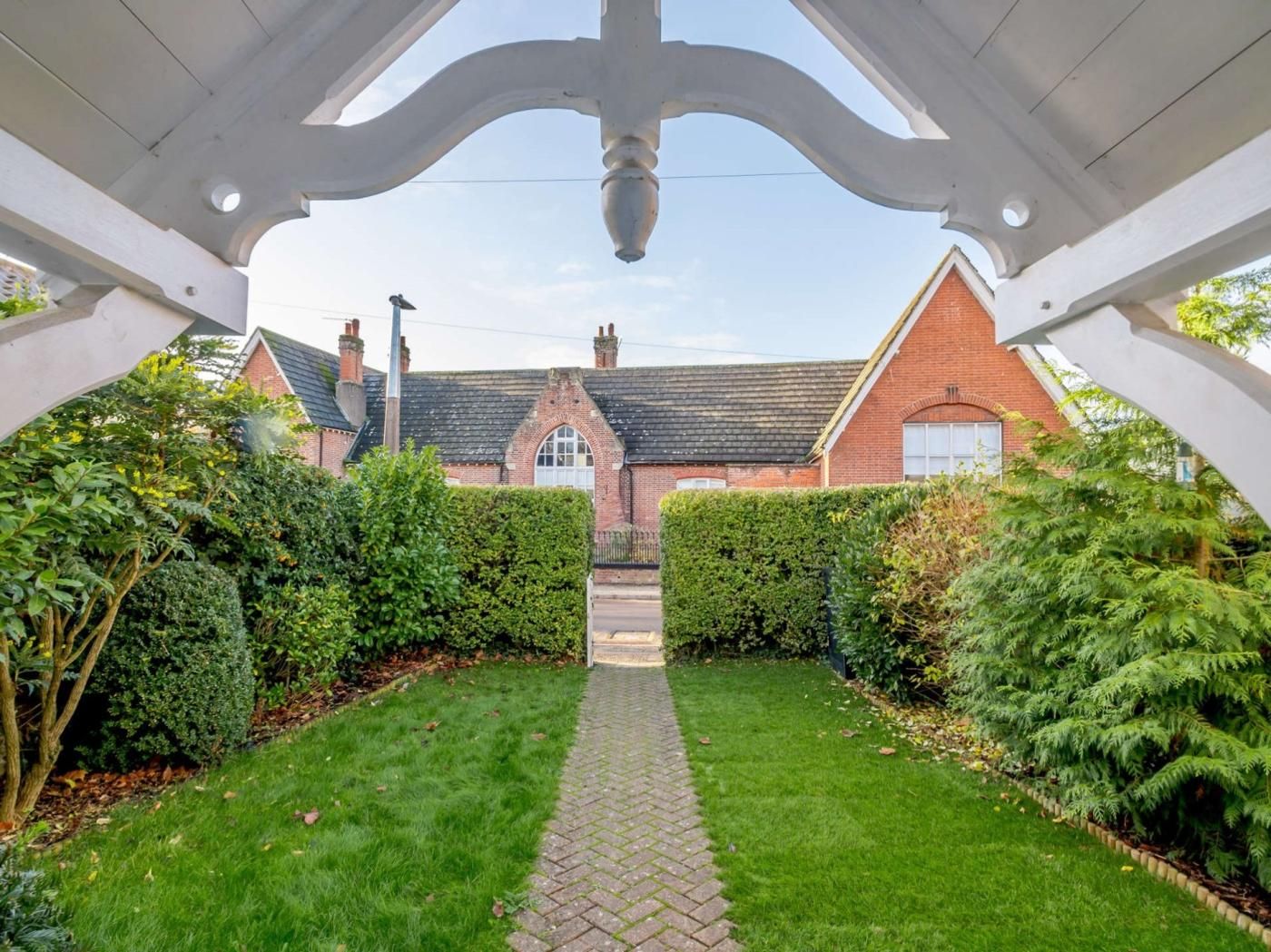 A garden pathway leading to a brick house with a gabled roof and a visible chimney.