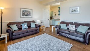 A living room with two leather sofas, a coffee table, a rug, a floor lamp, and a chandelier. - 3 Bed in Seahouses (oc-90727) (Seahouses)