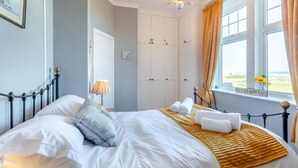 A neatly made bed with white linens, a bedside lamp, and a view of the sea through a window. - 3 Bed in Seahouses (oc-90727) (Seahouses)