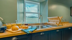 Una cocina con ventana, un lavabo, un escurreplatos y provisiones para el desayuno sobre la encimera.