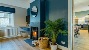 Una sala moderna con chimenea, una planta grande en maceta y vista a la cocina.