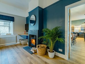 A modern living room with a fireplace, a large potted plant, and a view into the kitchen. - 4 Bed in Crieff (oc-90801) (Crieff)