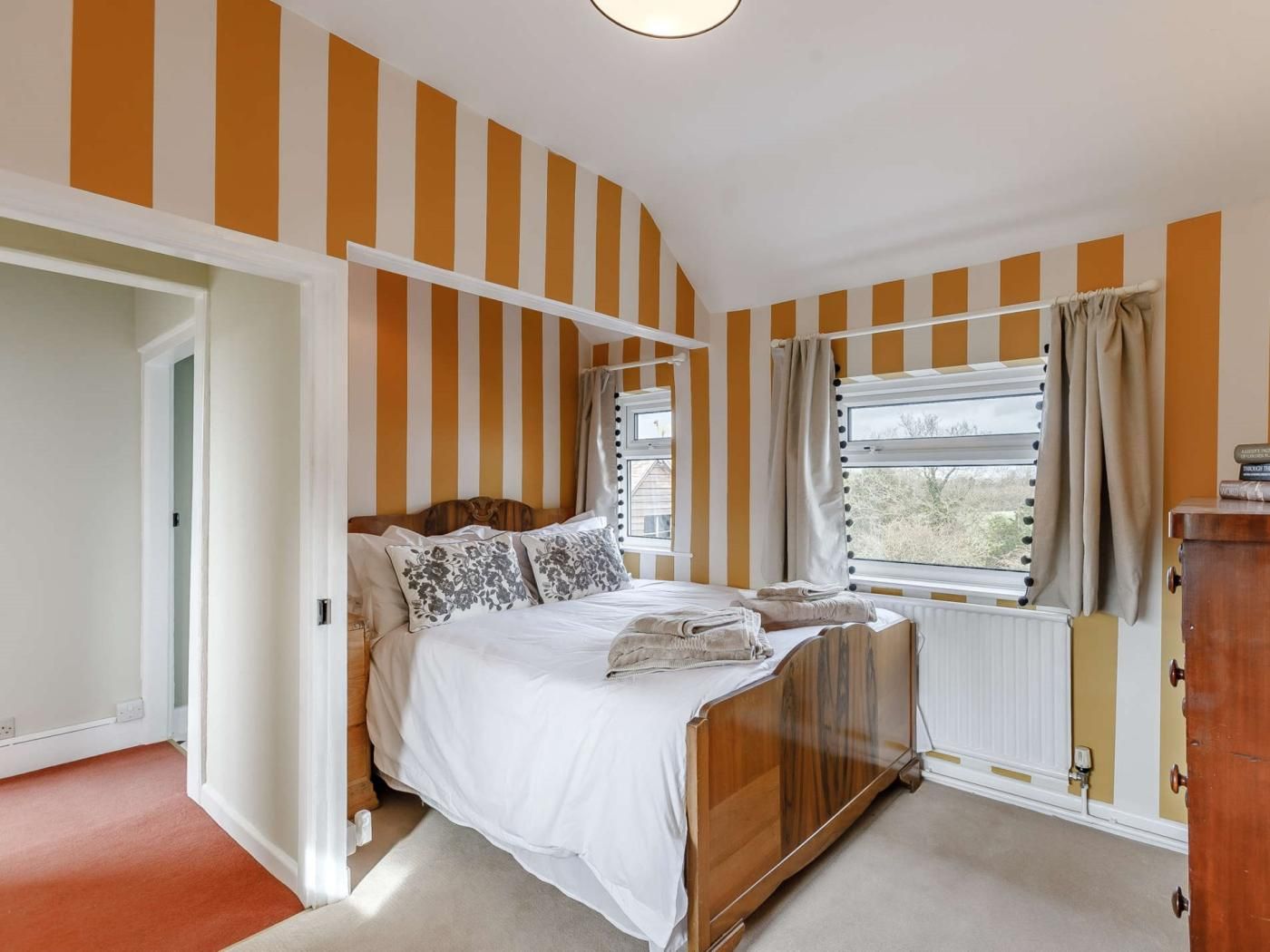 A bedroom with a wooden bed, striped walls, a window with curtains, and a radiator.