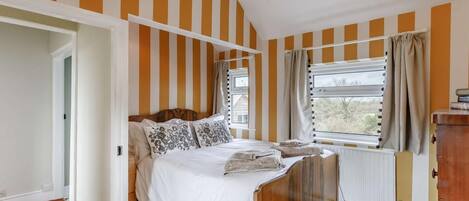 A bedroom with a wooden bed, striped walls, a window with curtains, and a radiator.