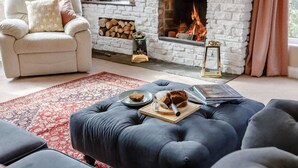 A cozy living room with a fireplace, a plush armchair, a blue ottoman, and a red patterned rug. - 3 Bed in Malvern (oc-90775) (Mathon)