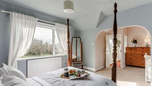 A bedroom with a four-poster bed, a large window with curtains, a radiator, and a dresser with a mirror. - 3 Bed in Malvern (oc-90775) (Mathon)