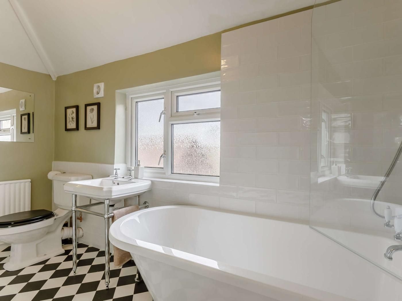 A bathroom with a white bathtub, a sink, and a toilet. There is a window with frosted glass and a radiator on the wall.